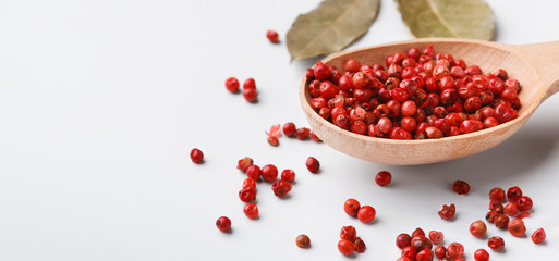 Red peppercorn balls in wooden spoon on white background