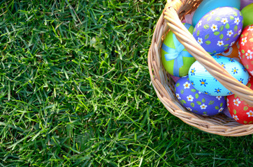 Flat lay shot of Easter eggs in the wicker basket on green spring grass. Space for text