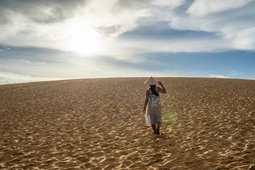 Woman Walking towards the Sun in the Red Sand Dunes in Vietnam