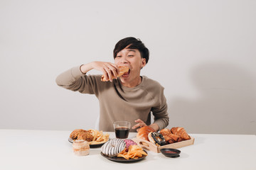 Portrait of asian man sitting and snacking donuts isolated over white background. Fat man diet...