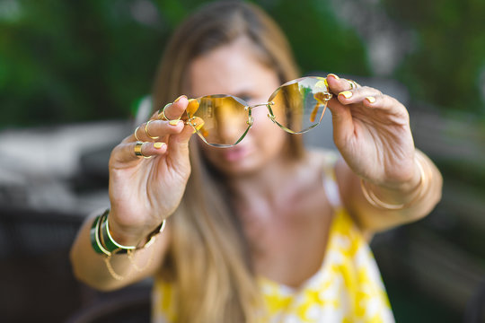 Young woman holding yellow sunglasses in her hands in front of camera. Still of stylish accessories
