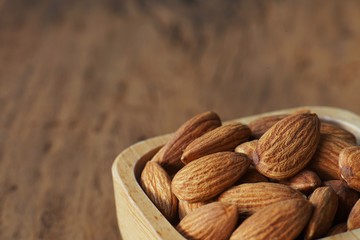 Almond nut in wooden bowl on wooden table with green leaf background