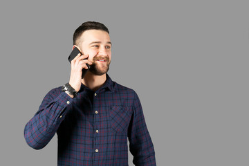 Young handsome man with facial hair holding posing over gray wall with a lot of copy space for text. Portrait of confident bearded male, wearing hipster slim fit checkered shirt. Isolated, background.