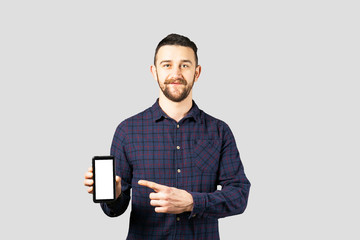 Young handsome man with facial hair holding posing over gray wall with a lot of copy space for text. Portrait of confident bearded male, wearing hipster slim fit checkered shirt. Isolated, background.