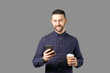 Young handsome man with facial hair holding posing over gray wall with a lot of copy space for text. Portrait of confident bearded male, wearing hipster slim fit checkered shirt. Isolated, background.