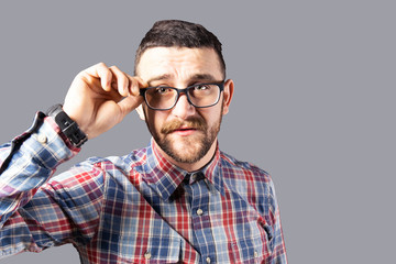 Obraz premium Young handsome man with facial hair holding posing over gray wall with a lot of copy space for text. Portrait of confident bearded male, wearing hipster slim fit checkered shirt. Isolated, background.