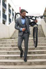 Confident young businessman carrying his bicycle while walking outdoors.