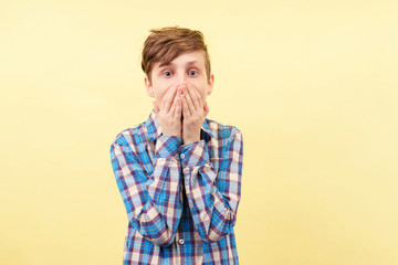 overexcited joyful happy smiling boy covering mouth with hands over yellow background, advertisement, banner or poster template, emotion facial expression, people reaction