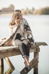 Attractive woman drinking coffe or tea at the pier outdoors