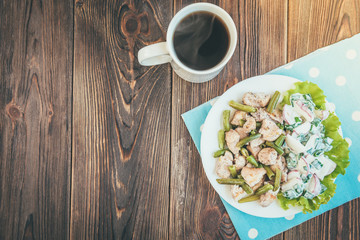 Baked chicken pieces with green beans and salad of green onion and red radish on wooden background.