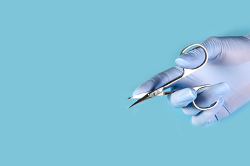 master nails in blue gloves holds manicure tool scissors. set of manicure accessories on blue...
