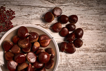 group of tasty chestnuts next to a bowl on an old wooden board
