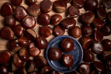 group of tasty chestnuts next to a bowl on an old wooden board
