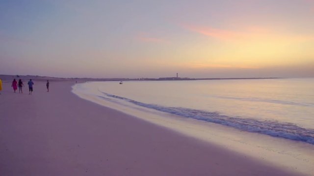 People walking on shivrajpur beach dwarka gujarat at dusk blue hour with waves and beautiful sky and water. The blue light, amazing gold and red dusk sky, blue water and silhouette of families on this