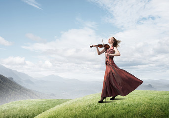 Woman violinist in red dress playing melody against cloudy sky © adam121