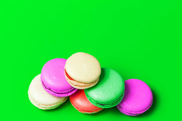 Top view of colorful pink, beige, red sweet macaroons on green background with copy space