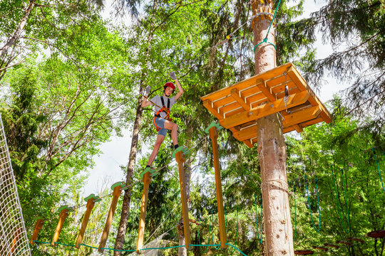 Teen boy on a ropes course in a treetop adventure park passing hanging rope obstacle