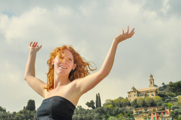 Freudig glückliches Portrait einer jungen eleganten rothaarigen lockigen Frau mit erhobenen Armen...