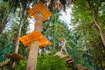 Teen boy on a ropes course in a treetop adventure park passing hanging rope obstacle
