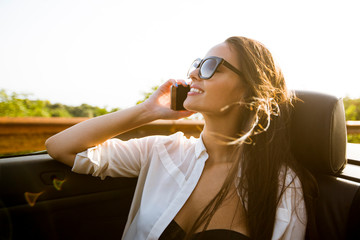 Woman uses mobile phone and siting in cabriolet at summer day