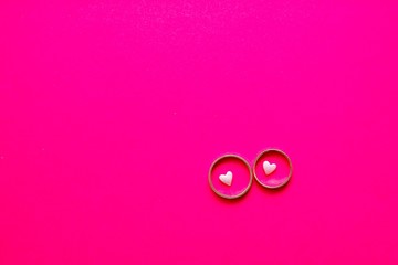 Love and marriage concept. Valentine's Day. Two golden wedding rings with small light pink hearts within on bright pink background with copy space