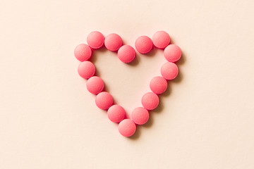 Obraz premium Pink pills in the shape of a heart on a light background