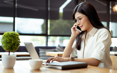 Happy Freelancer asian woman talking customer with smartphone about working job recive order using digital laptop computer on workspace