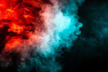 Translucent, thick smoke, illuminated by light against a dark background, divided into two colors: blue and red, burns out, evaporating from a pair of vape.