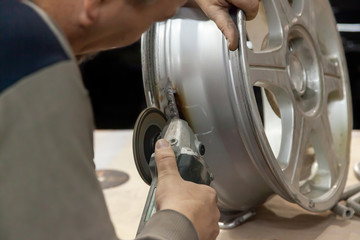 The repairman holds in his hands a special tool like a grinder, levels the cast disk in the...