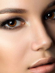 Naklejka premium Close up beauty portrait of young woman with golden makeup. Perfect skin and fashion makeup, smokey eyes. Studio shot. Sensuality, passion and skincare concept. Extreme closeup, partial face view