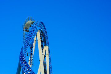 Steep ride on a roller coaster in a park against a blue sky.