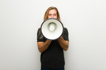 Blond man with long hair over white wall shouting through a megaphone to announce something