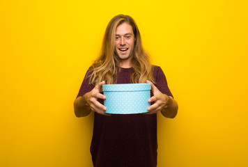 Blond man with long hair over yellow wall surprised because has been given a gift