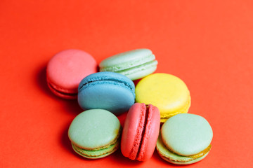 Close-up of sweet green, yellow, coral, blue macaroons on red background