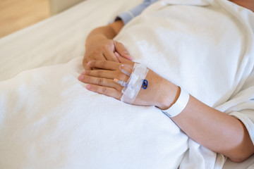 Closeup of hands with intravenous (IV) man patient in hospital bed.