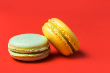 Close-up of two green and yellow French macaroons on a red background
