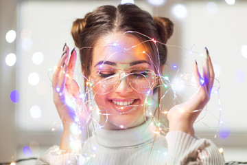 Young woman with glasses and christmas lights smiling