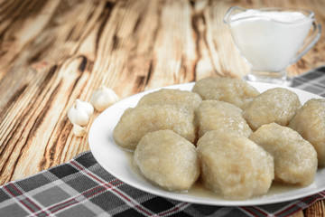 Potato dumplings with stuffed minced meat on a white plate and gravy boat with sour cream on wooden background.