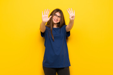 Young woman with glasses over yellow wall counting nine with fingers