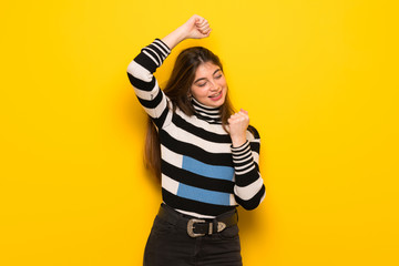 Young woman over yellow wall celebrating a victory