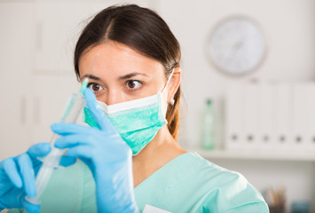 Female nurse in mask holding syringe for injection in hospital