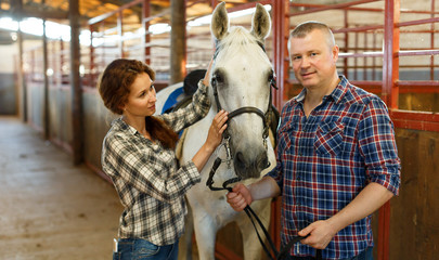 Couple of farmers  standing  with white horse  at stabling indoor