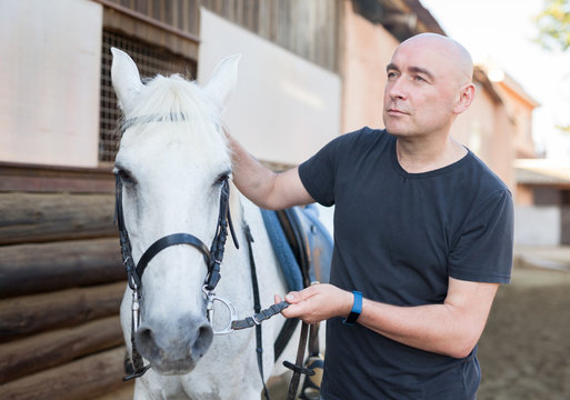 Mature Smiling Man Farmer Standing  With White Horse At  Stable