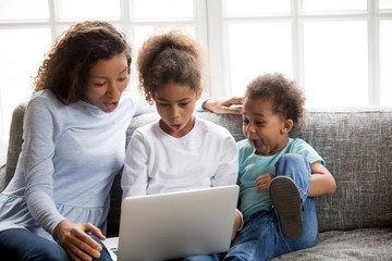 Excited african american mom and mixed race kids looking at laptop surprised with unbelievable online news, amazed black family mother children astonished by huge shopping sale or special email offer