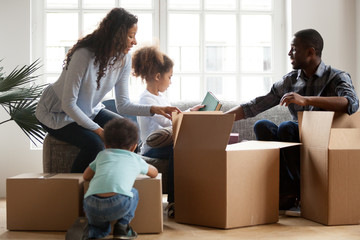 Fototapeta na wymiar African american kids helping parents unpacking boxes in living room together, afro parents and mixed race children packing stuff preparing to relocate, black family in new home on moving day
