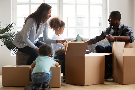 African american kids helping parents unpacking boxes in living room together, afro parents and mixed race children packing stuff preparing to relocate, black family in new home on moving day