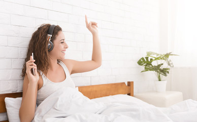 Happy woman in headphones listening to music fin bed