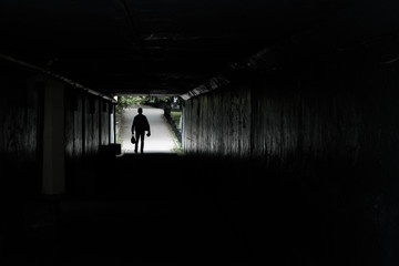 Fototapeta na wymiar silhouette of a walking man at the end of the tunnel, in the hands of men bags and packages, background road pedestrian