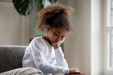 Upset little african american girl feels hurt sad bored sitting alone at home, depressed punished mixed race kid having psychological trauma, frustrated preschool black child thinking hiding problem - Powered by Adobe