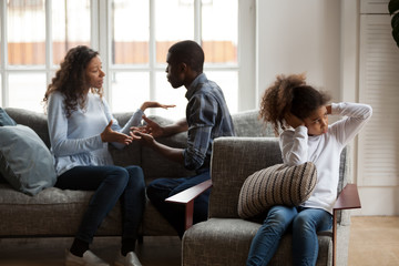 Upset african american kid daughter closing ears not listening to noisy shouting parents fighting arguing at home, sad preschool mixed race child girl stressed with mom and dad black family conflict